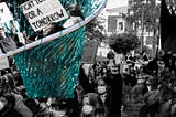Black and white photo of people protesting in masks. A turquoise net has scooped some up from above.