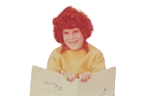 Adva Shaviv at age 7, smiling while holding up a book.