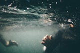 Two people are partially visible, submerged in dark, turbulent water