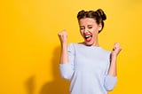 Ecstatic woman saying ‘Yeah’ with fists clenched, on a bright yellow background.