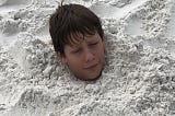 young boy buried in sand at the beach