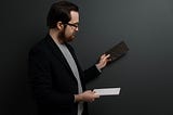 A man in a suit jacket holding up two different blocks and tiles and looking in comparison