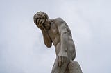 A statue of a male doing a face-palm against a cloudy-sky background