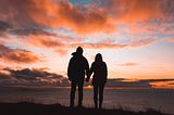 Photo of couple holding hands facing a beautiful sunset.