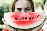 Smiling young woman holding a big watermelon “smile” in front of her mouth
