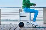 Person riding on a three-wheel electric suitcase.