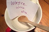 Mixing bowl and wooden spoon with a piece of paper inside that says “Write. Write. Write.”