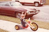 Author as a child riding a big wheel on a neighborhood sidewalk, circa 1980s.