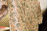 A small floral baby onesie on a hanger being held up indoors.