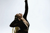 Black woman sitting on white floor in black bodysuit posing with a self-tie rope harness