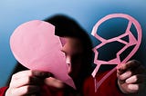 Person holding two parts of a paper heart.