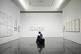 A child sitting on a bench in a minimalist art gallery.