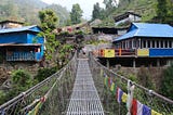 Me waving and standing on the other side of a suspension bridge in Nepal