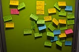 A board covered with colourful post-it notes, the title says “feedback please” and it consists of notes suggesting improvements for BarCamp Manchester.