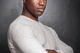 A man standing with his arms crossed in front of a grey background