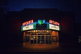 A movie theater after dark, after closing. The neon sign advertising the feature films.