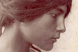 A vintage black and white photograph of a young, dark-haired woman with eyes fixed on something to the right of the frame.