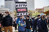 A woman with a blue jacket on showing a placard “Stop Asian Hate” amidst a group of people staging a peaceful protest.