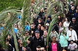 A diverse crowd of people walk carrying palms in a Palm Sunday procession.