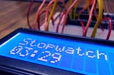 An electronics circuit on a breadboard with an LCD displaying the words “Stopwatch 03 minutes 29 seconds”