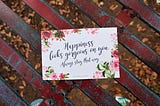 A card with a quote on happiness placed on a wooden bench