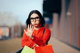 Woman holding shopping bags makes stop sign with her hand.