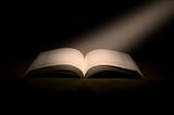 A shaft of light falls on the open pages of a book against a black background.