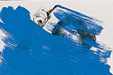 Fotografia de uma mulher com tinta azul (que ela está pintando) cobrindo a maior parte da imagem