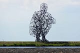 “Exposure” by Antony Gormley, a large sculpture depicting a hollow crouching person, made of straight pieces of metal bolted together.