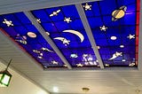 Blue stained glass in a ceiling with cartoon-style planets and stars on it.