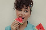 A woman putting a piece of watermelon in her mouth.