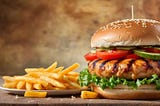 A delicious Hamburger stacked with lettuce, tomatoes and pickles next to a plate of crunchy salted french fries. Yumm.