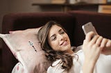 Woman in White Top Holding Smartphone Lying on Couch