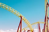 A close-up of red and yellow roller coaster against a blue sky