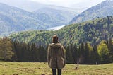 A woman contemplates a mountain landscape.