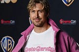Ryan Gosling in a white shirt that reads “From Director Greta Gerwig” in the iconic Barbie font. Under a pink jacket to boot.