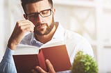 A man with a sad expression reading a red book.