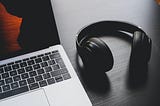 An open MacBook and a pair of wireless headphones rest on a work desk.