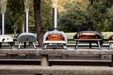A lineup of several Ooni pizza ovens with the Fyra 12 on the far left, and the Ooni Karu 16 in the middle.