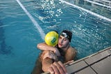 Na imagem tem dois jovens se abraçando, um deles é o Adenilson e o outro o José Arthur. Ambos estão dentro de uma piscina para natação. Adenilson está usando uma touca de natação amarela com a bandeira do Brasil. José Arthur está usando uma touca preta e um óculos de natação na cabeça.