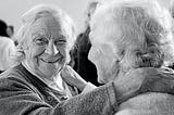 Two elderly women embracing themselves happily