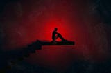 A person sitting on a staircase in a dark dystopian area backlit by an ominous intensely bright crimson red light.