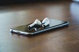 A pair of Apple air pods and an iPhone sitting on a table happily paired together