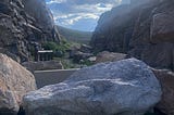 A mountain pass with partly cloudy blue skies is blocked by large boulders.