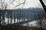 winter photo of Severn River bridge through the leafless trees, with it’s reflection on the water