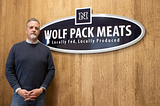 Tom Kulas standing in front of a Wolf Pack Meats sign.
