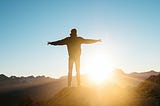 A man standing on the mountain with open arms looking at the sunsire
