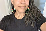 Dr. Kimya with locs, long earrings, and a 365 Diversity shirt sold on (Tee)Spring that states “Black Health is Holistic.”