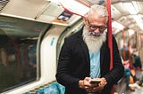 Older hipster man looks at phone on subway
