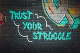 ‘Trust Your Struggle’ graffitied in bright green on to a painted black brick wall